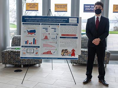 A student wearing a suit standing next to a poster presentation 